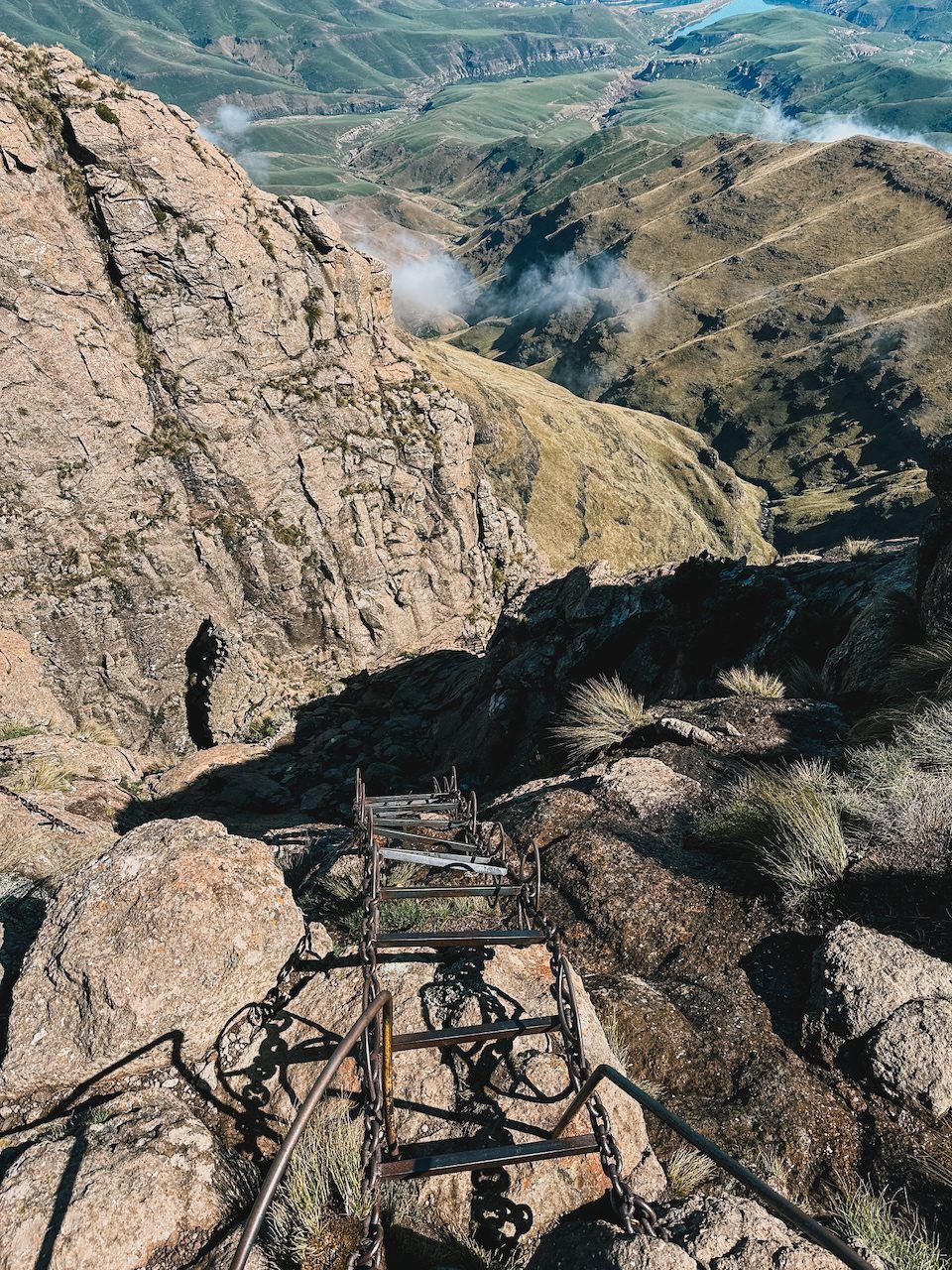 Chain ladder down a rock face, green valleys far below
